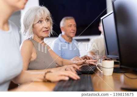 Portrait of an elderly positive woman working on computer with group of friends while attending PC classes in nursing home Portrait of an elderly positive woman working on computer with group of friends while attending PC classes in nursing home 139815675