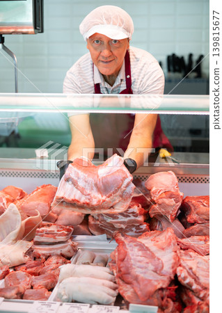 Adult man seller lays out pork in butcher shop Adult man seller lays out pork in butcher shop 139815677