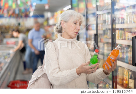 Aged woman choosing refreshing beverages in grocery store Aged woman choosing refreshing beverages in grocery store 139815744