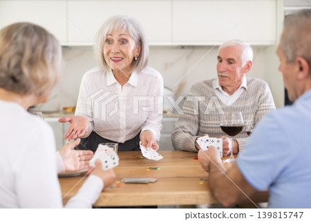 Cheerful friendly company of men and women sitting at kitchen table and enjoying the poker game. Friends play card game at home. Evening entertainment concept Cheerful friendly company of men and women sitting at kitchen table and enjoying the poker game. Friends play card game at home. Evening entertainment concept 139815747