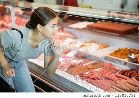 Young girl choosing raw meat in display case of butcher shop Young girl choosing raw meat in display case of butcher shop 139815751