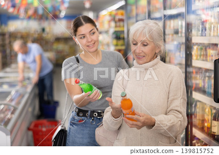 Elderly woman and young girl choosing soft drinks in store Elderly woman and young girl choosing soft drinks in store 139815752