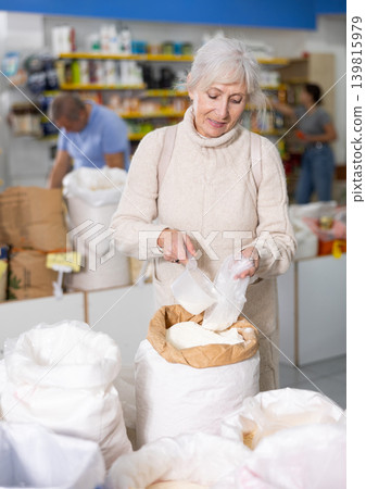 Aged woman filling plastic bag with wheat flour in food store 139815979