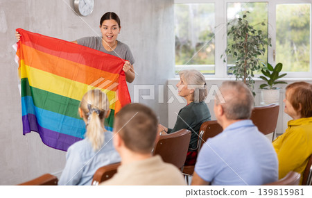 Portrait of young female teacher conducting lesson for adult students, talking about LGBT community and showing rainbow flag Portrait of young female teacher conducting lesson for adult students, talking about LGBT community and showing rainbow flag 139815981