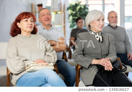 Interested group of people of different ages sitting on chairs and listening lecture in conference hall 139816027