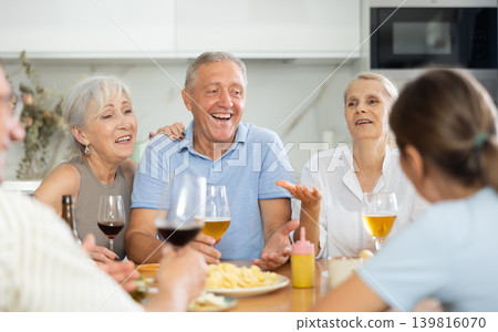 Joyful elderly women and man chatting and drinking at kitchen table Joyful elderly women and man chatting and drinking at kitchen table 139816070