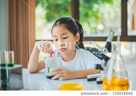 little scientist looking through a microscope and test tubes filled with chemicals for learning about science and experiments. little scientist looking through a microscope and test tubes filled with chemicals for learning about science and experiments. 139816088