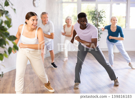 Female instructor teaches mature students of dance class basic movements of hip hop dance Female instructor teaches mature students of dance class basic movements of hip hop dance 139816183