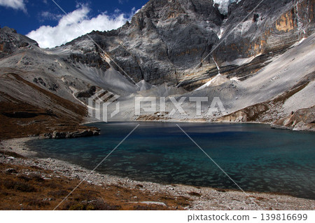 A tranquil alpine lake spreads out beneath rugged cliffs. A tranquil alpine lake spreads out beneath rugged cliffs. 139816699