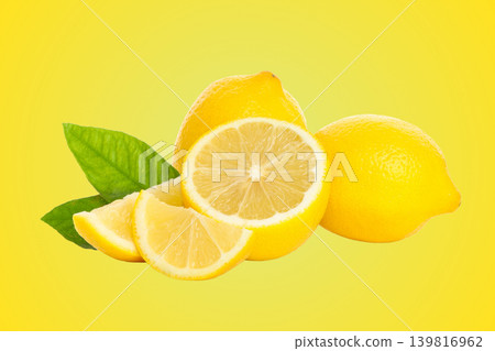 Two whole lemons with a sliced lemon and green leaves nearby 139816962