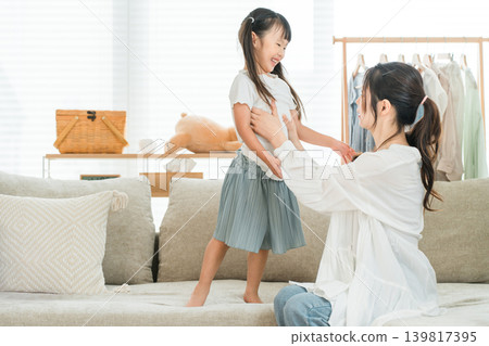 一位母親在家裡的客廳幫女兒穿衣服 一位母親在家裡的客廳幫女兒穿衣服 139817395