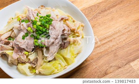 Steamed pork and cabbage in a frying pan, placed on a wooden table. Steamed pork and cabbage in a frying pan, placed on a wooden table. 139817483