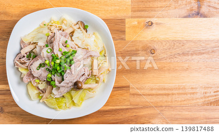 Steamed pork and cabbage in a frying pan, placed on a wooden table. Steamed pork and cabbage in a frying pan, placed on a wooden table. 139817488