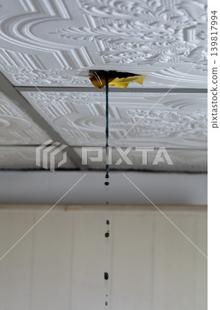 Water leaking through damaged ceiling tile inside house during rainstorm. Ceiling water leak from broken roof or pipe inside residential home 139817994