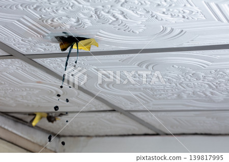Water leaking through damaged ceiling tile inside house during rainstorm. Ceiling water leak from broken roof or pipe inside residential home Water leaking through damaged ceiling tile inside house during rainstorm. Ceiling water leak from broken roof or pipe inside residential home 139817995