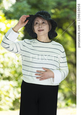 一位戴著帽子的老婦人在綠樹環繞的公園散步。 139818058