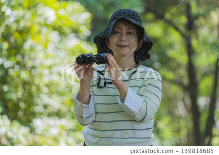 一位老婦人在綠樹環繞的公園裡用望遠鏡觀鳥。 139818685
