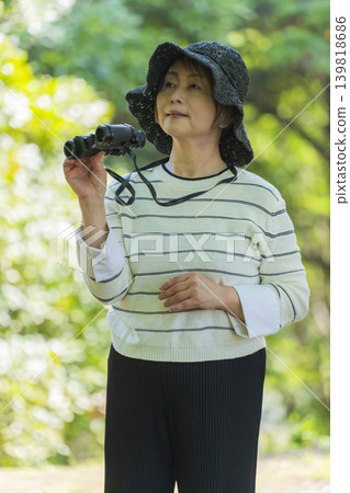 一位老婦人在綠樹環繞的公園裡用望遠鏡觀鳥。 一位老婦人在綠樹環繞的公園裡用望遠鏡觀鳥。 139818686