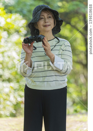 一位老婦人在綠樹環繞的公園裡用望遠鏡觀鳥。 一位老婦人在綠樹環繞的公園裡用望遠鏡觀鳥。 139818688