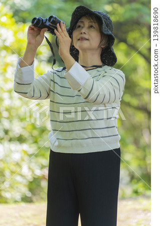 一位老婦人在綠樹環繞的公園裡用望遠鏡觀鳥。 139818690