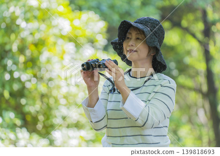 一位老婦人在綠樹環繞的公園裡用望遠鏡觀鳥。 一位老婦人在綠樹環繞的公園裡用望遠鏡觀鳥。 139818693