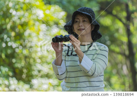 一位老婦人在綠樹環繞的公園裡用望遠鏡觀鳥。 一位老婦人在綠樹環繞的公園裡用望遠鏡觀鳥。 139818694