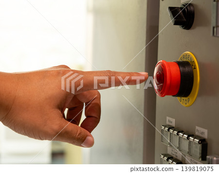 Close up of operator hand reaching emergency stop button on industrial control panel in factory environment, representing workplace safety, machine shutdown system and industrial protection Close up of operator hand reaching emergency stop button on industrial control panel in factory environment, representing workplace safety, machine shutdown system and industrial protection 139819075