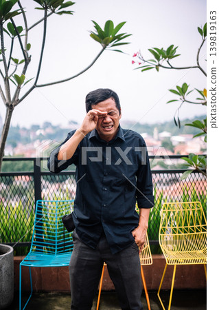 Man Rubbing His Eye With a Pained Expression Outdoors Man Rubbing His Eye With a Pained Expression Outdoors 139819163