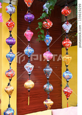 Colorful traditional Hoi An silk lanterns with floral patterns hanging in rows against yellow wall at outdoor souvenir market in Vietnam Colorful traditional Hoi An silk lanterns with floral patterns hanging in rows against yellow wall at outdoor souvenir market in Vietnam 139819299