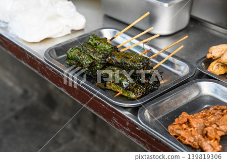 Traditional Vietnamese grilled Bo La Lot beef wrapped in lolot leaves on skewers is displayed on a metal tray at a street food stall in Vietnam Traditional Vietnamese grilled Bo La Lot beef wrapped in lolot leaves on skewers is displayed on a metal tray at a street food stall in Vietnam 139819306