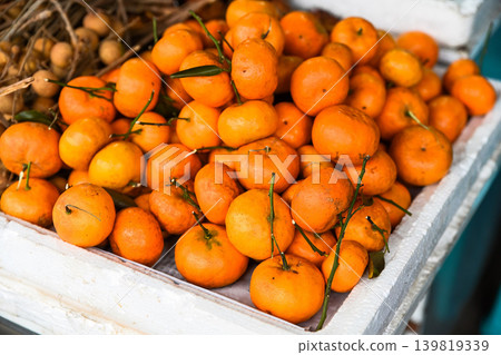 A close up view of fresh ripe quyt mandarin orange fruit with green stem displayed at a traditional street fruit market stall in Hoi An Vietnam 139819339