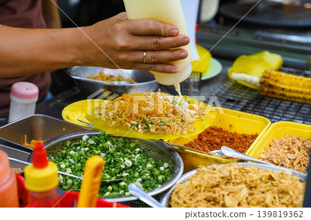 Vendor hand squeezing white sauce from plastic bottle onto traditional Vietnamese street food rice paper pizza banh trang nuong at outdoor stall Vendor hand squeezing white sauce from plastic bottle onto traditional Vietnamese street food rice paper pizza banh trang nuong at outdoor stall 139819362