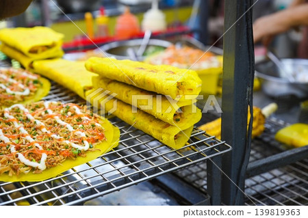 Traditional crisp yellow savory pancakes and vietnamese rice paper pizza displayed on metal wire rack at outdoor street food market stall in Vietnam Traditional crisp yellow savory pancakes and vietnamese rice paper pizza displayed on metal wire rack at outdoor street food market stall in Vietnam 139819363