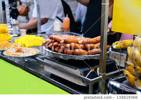 Grilled meat sausages piled on tray near traditional pancakes and corn cobs for sale at Asian outdoor street food market stall in Vietnam Grilled meat sausages piled on tray near traditional pancakes and corn cobs for sale at Asian outdoor street food market stall in Vietnam 139819366