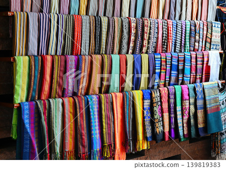 Traditional handmade colorful ethnic brocade fabrics and woven scarfs displayed in rows for sale at outdoor souvenir market in Vietnam Traditional handmade colorful ethnic brocade fabrics and woven scarfs displayed in rows for sale at outdoor souvenir market in Vietnam 139819383