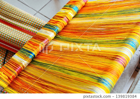Close up of bright colorful yellow and orange threads on traditional handloom weaving vibrant textile patterns at local workshop in Vietnam Close up of bright colorful yellow and orange threads on traditional handloom weaving vibrant textile patterns at local workshop in Vietnam 139819384