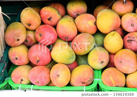 Fresh ripe colorful mango fruits piled inside green plastic crates for sale at traditional outdoor street market in Hoi An Vietnam Fresh ripe colorful mango fruits piled inside green plastic crates for sale at traditional outdoor street market in Hoi An Vietnam 139819389