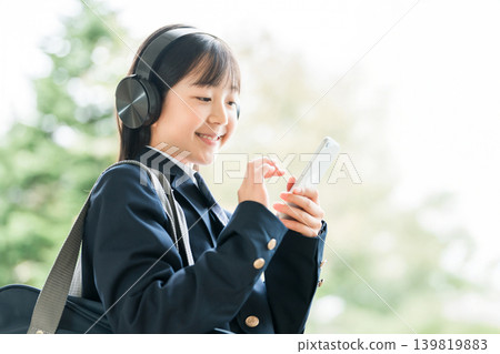 Elementary school, junior high school, and high school girls in uniforms listening to music with headphones in the school corridor Elementary school, junior high school, and high school girls in uniforms listening to music with headphones in the school corridor 139819883
