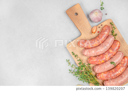 Raw sausages on wooden cutting board with herbs top view Raw sausages on wooden cutting board with herbs top view 139820207