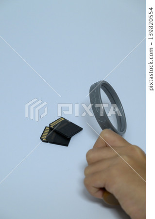 一隻手正用放大鏡檢查SD卡。 一隻手正用放大鏡檢查SD卡。 139820554