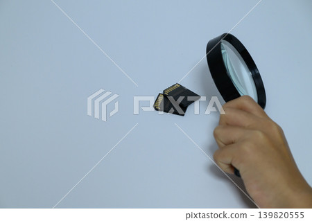 A person's hand examining an SD card with a magnifying glass. A person's hand examining an SD card with a magnifying glass. 139820555
