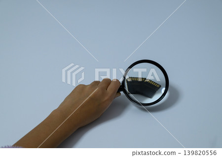 An SD card magnified with a magnifying glass and a human hand. An SD card magnified with a magnifying glass and a human hand. 139820556