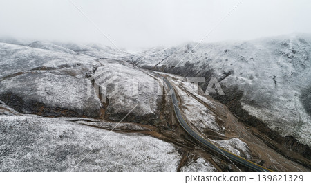 A single road cuts through the desolate winter mountains, lightly covered with snow. A single road cuts through the desolate winter mountains, lightly covered with snow. 139821329