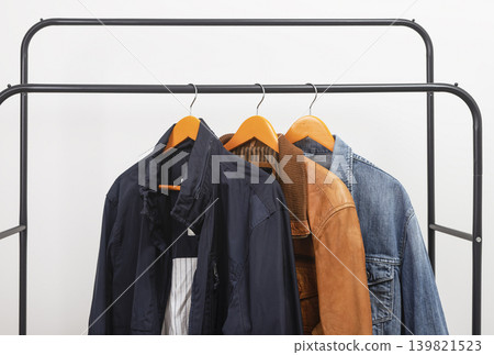 Several men jackets hanging on metal rack. Garments arranged on wooden hangers along rail. Menswear outerwear assortment for seasonal wardrobe selection.. Several men jackets hanging on metal rack. Garments arranged on wooden hangers along rail. Menswear outerwear assortment for seasonal wardrobe selection.. 139821523