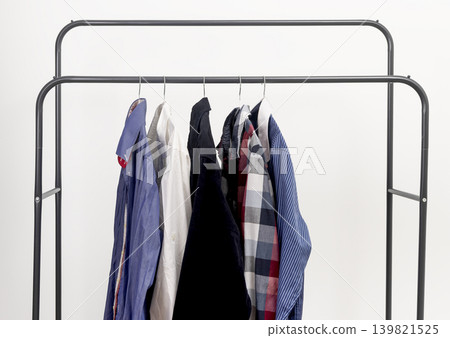 Several men shirts hanging on metal rack. Garments suspended on hangers along rail. Male wardrobe clothing collection for organized outfit selection.. Several men shirts hanging on metal rack. Garments suspended on hangers along rail. Male wardrobe clothing collection for organized outfit selection.. 139821525