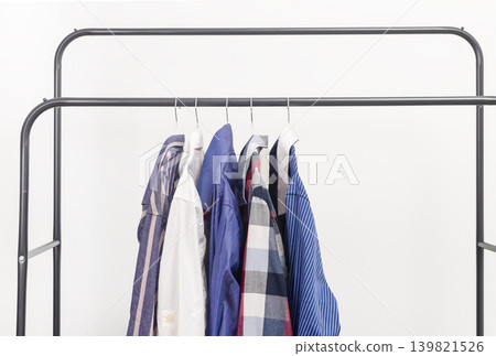 Several shirts hanging on metal clothing rack. Garments suspended from hangers on rail. Male wardrobe shirt collection concept.. Several shirts hanging on metal clothing rack. Garments suspended from hangers on rail. Male wardrobe shirt collection concept.. 139821526