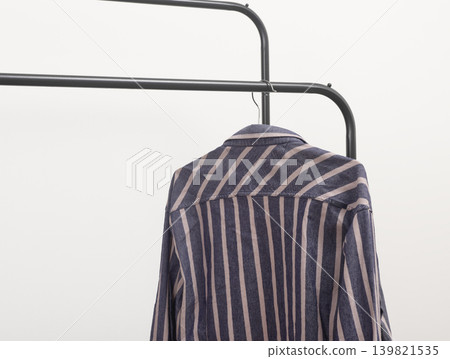 Striped shirt placed on curved rack. Apparel draped over metal hanger. Fashion storage wardrobe planning concept.. Striped shirt placed on curved rack. Apparel draped over metal hanger. Fashion storage wardrobe planning concept.. 139821535