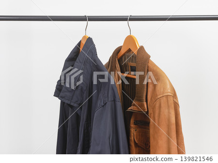 Two jackets hanging on clothing rack. Garments suspended from wooden hangers. Menswear outerwear selection for seasonal wardrobe.. Two jackets hanging on clothing rack. Garments suspended from wooden hangers. Menswear outerwear selection for seasonal wardrobe.. 139821546