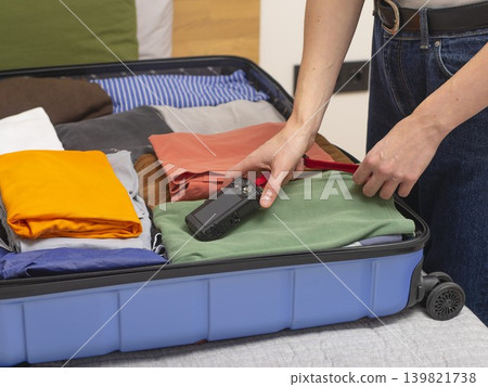 Open suitcase with clothes and camera on bed during packing. Indoor travel preparation scene showing Open suitcase with clothes and camera on bed during packing. Indoor travel preparation scene showing 139821738