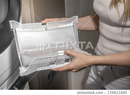 Hands holding and cleaning dryer lint filter, removing dust and dirt from compartment. Hands holding and cleaning dryer lint filter, removing dust and dirt from compartment. 139821800